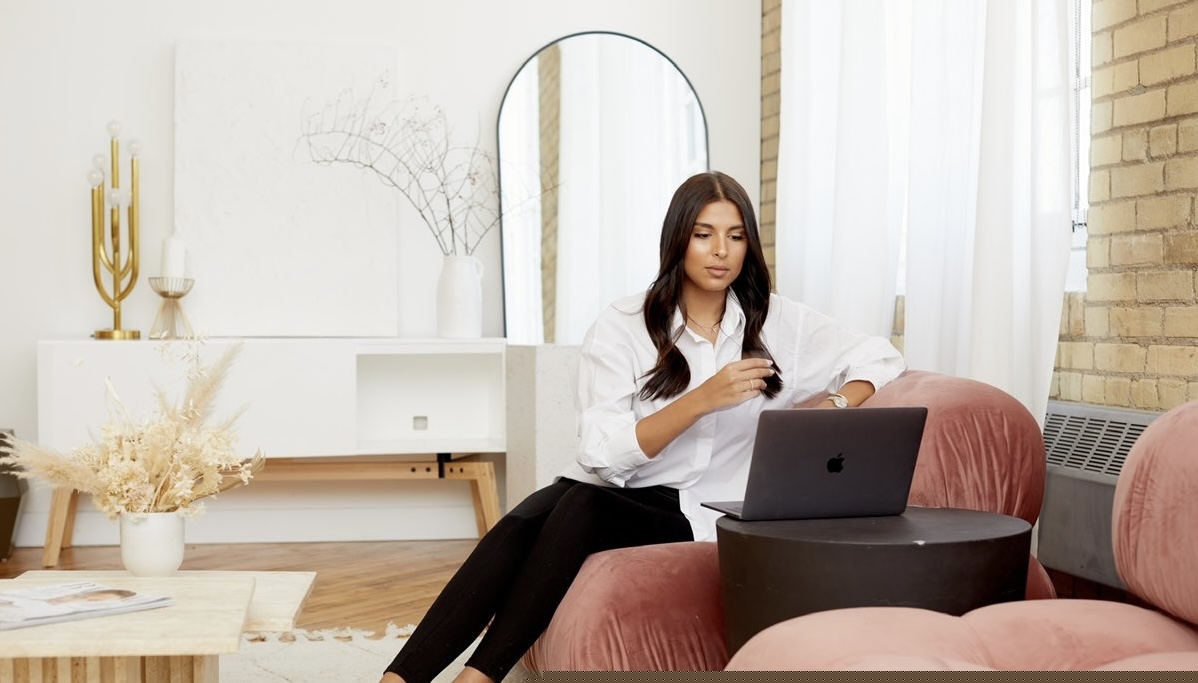 Woman looking at her laptop while sitting on a pink couch in a well-lit room